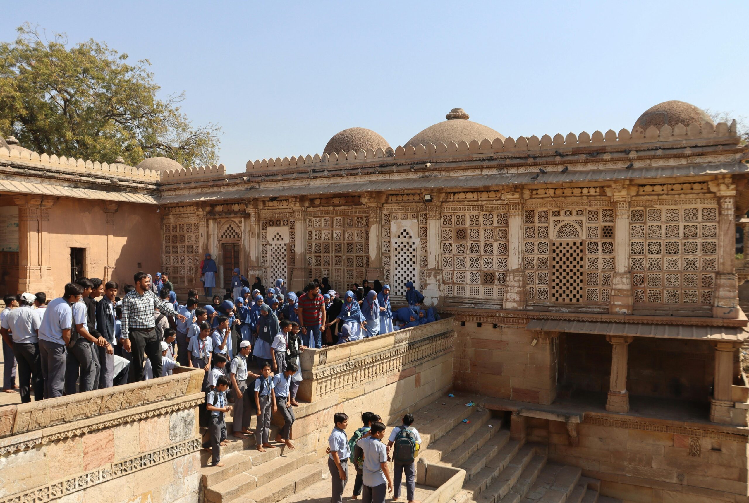 Schools & Educational Institutions A gathering of people in traditional attire at a historic Mughal architecture site during daytime in India.