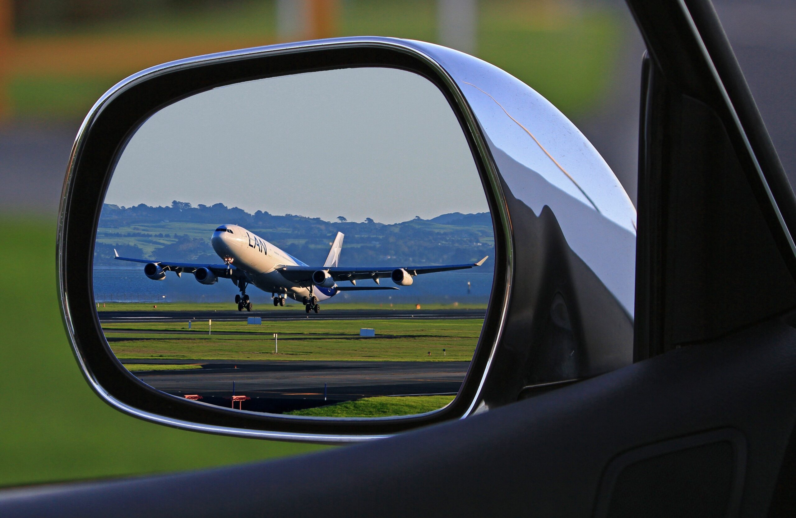 Corporate Travel A jet airplane taking off is reflected in a car's side mirror, capturing a unique aviation perspective.
