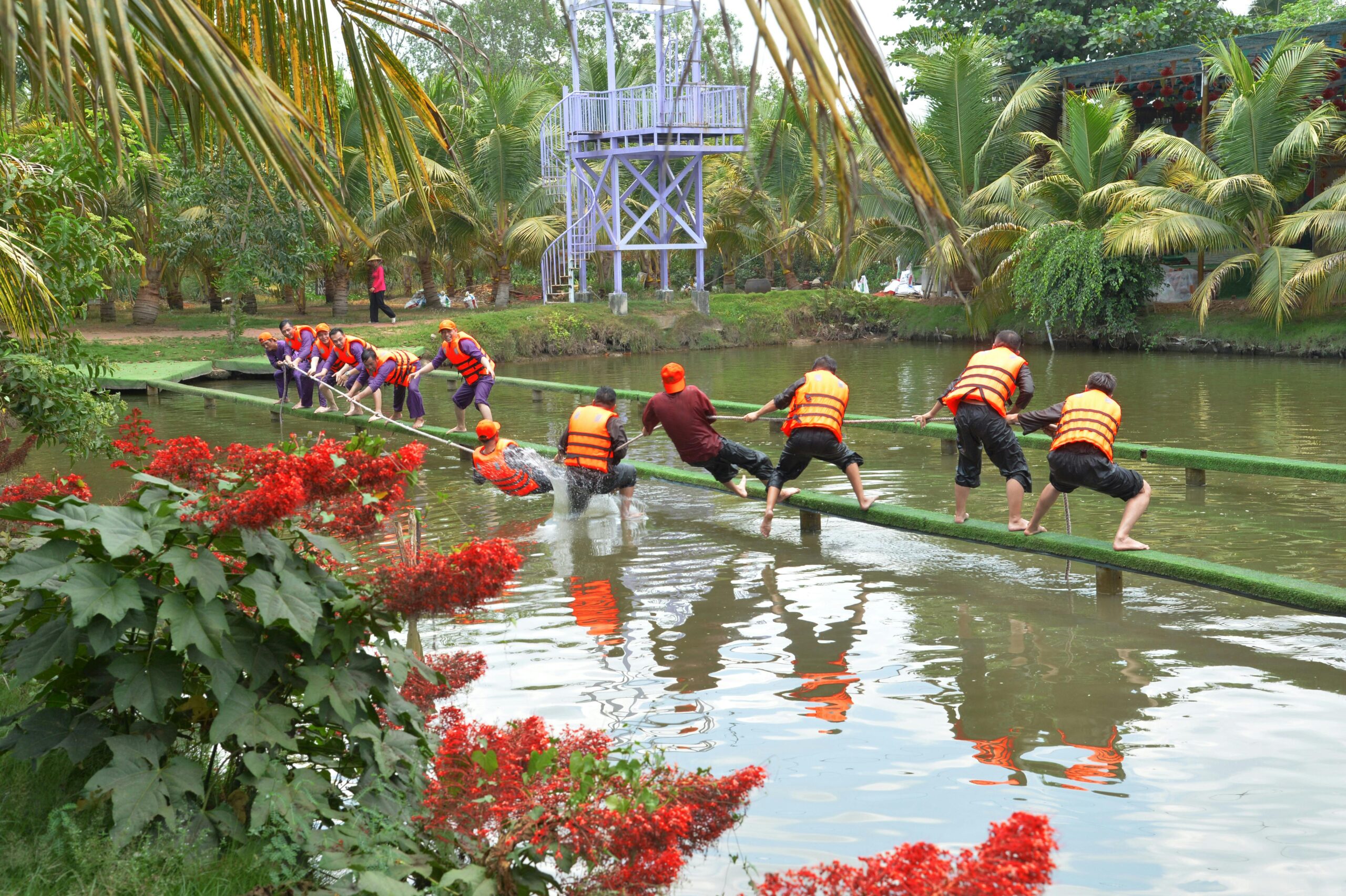 Corporate Travel A group of adults crossing a water obstacle course in an outdoor team building exercise.