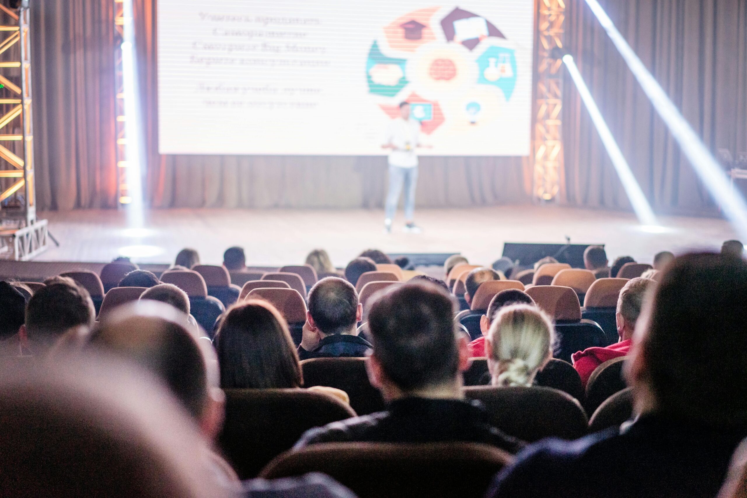 Corporate Travel Audience attentively watching a presentation in a conference setting, with stage lights and speaker visible.